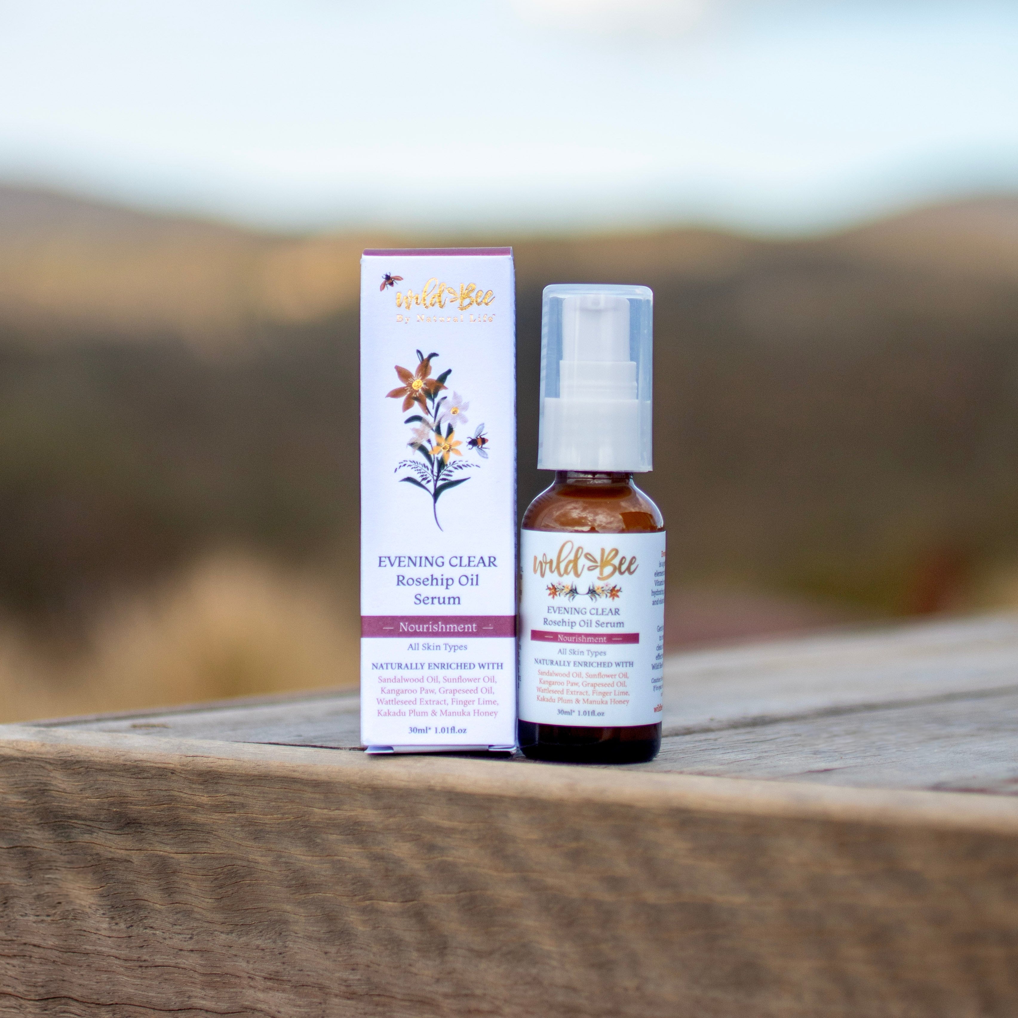 Wild Bee Evening Clear Serum on a natural product on a wooden surface with a blurred outdoor background