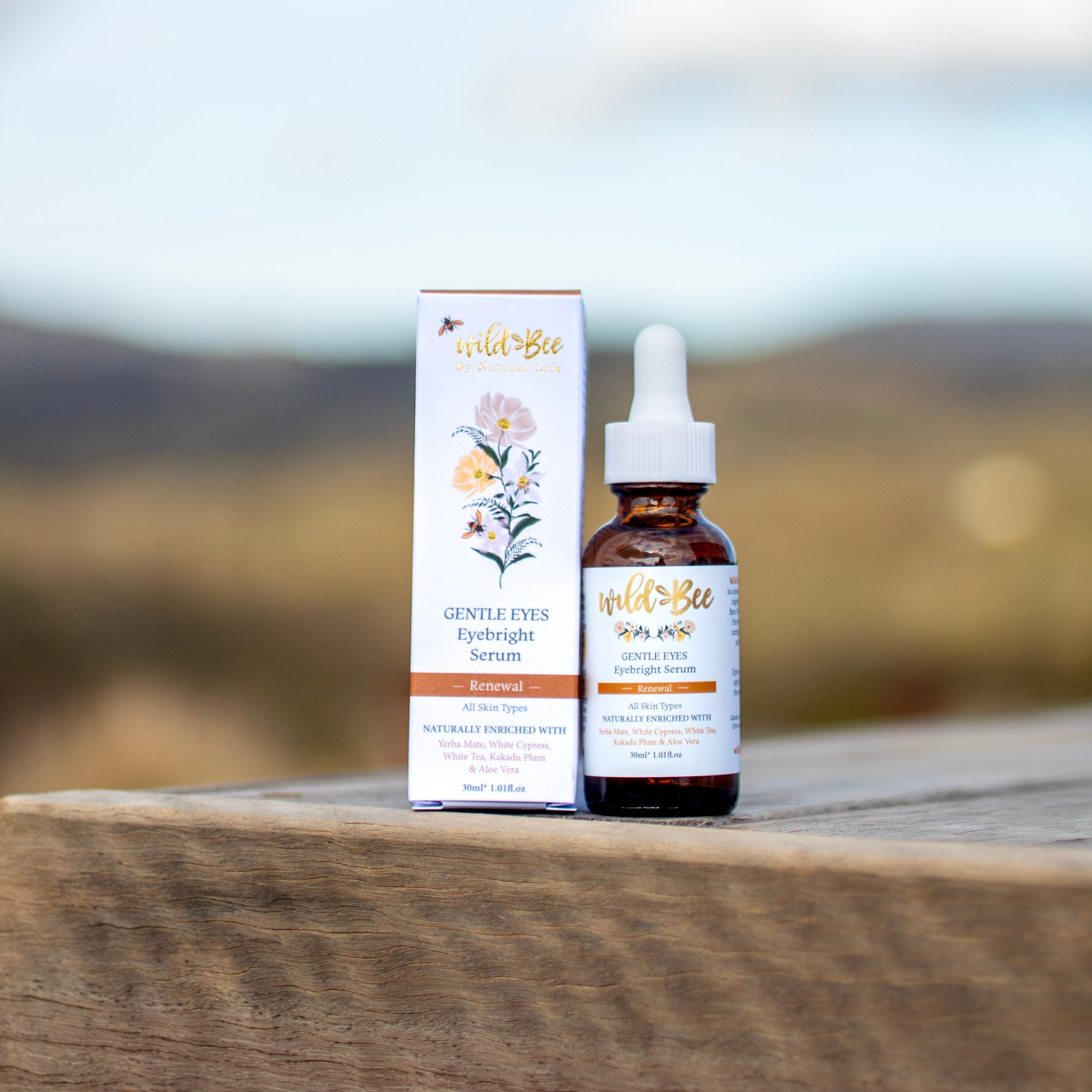 Bottle and box of Wild Bee Gentle Eyes Serum on a wooden surface with a blurred natural background