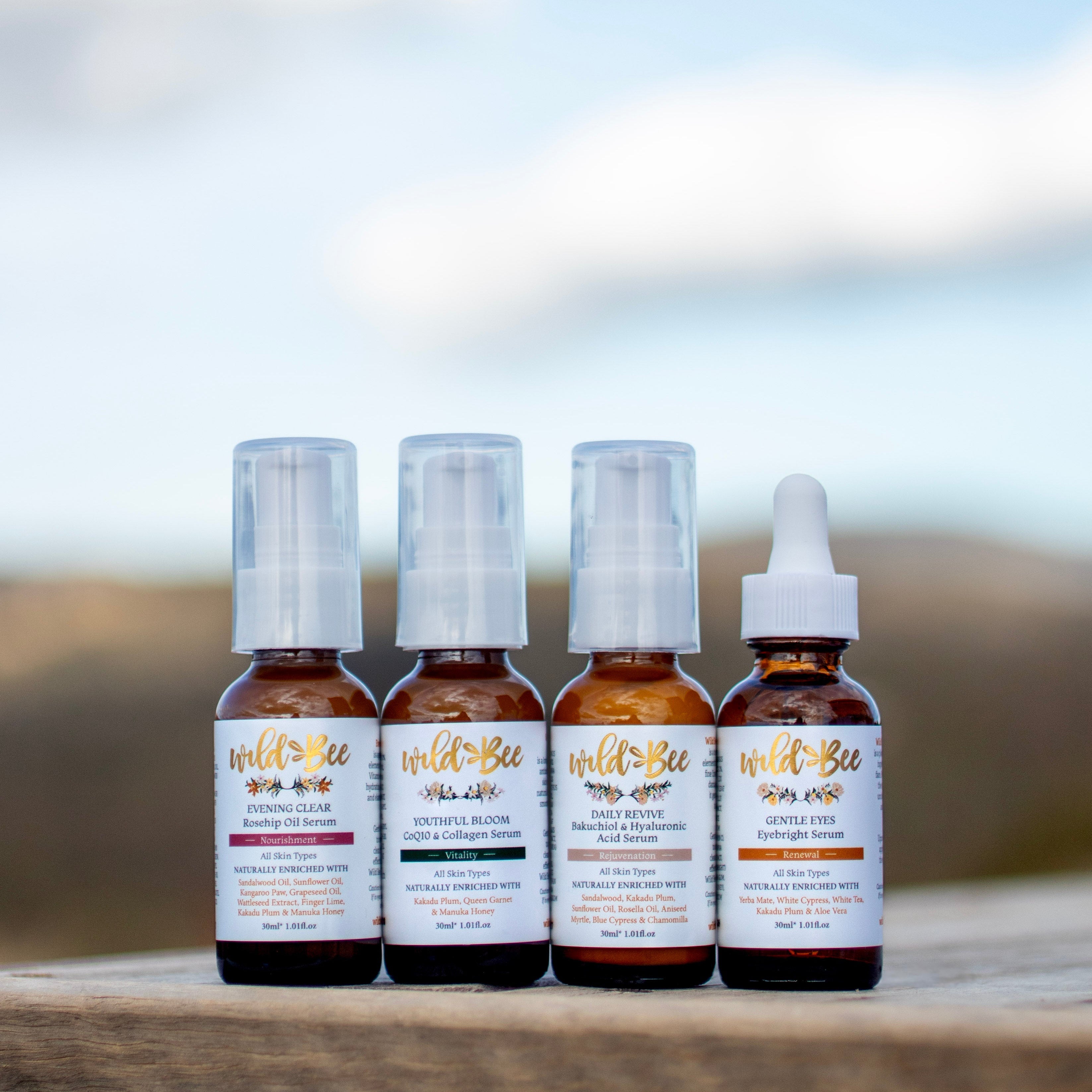 Four bottles of Wild Bee Skin + Body products on a wooden surface with a blurred natural background
